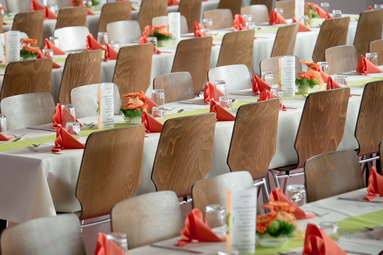 hero-img-01 Beautifully arranged tables with wooden chairs for a formal event, adorned with orange flowers.