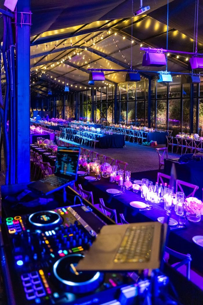 A vibrant indoor evening event with DJ equipment and elegantly lit tables creating a festive atmosphere.